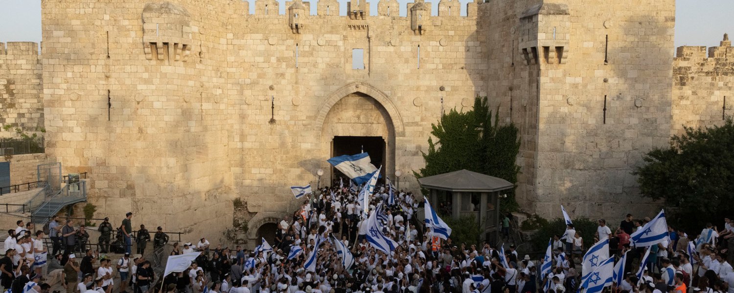 Israelis carrying blue-and-white Israeli flags march through Damascus Gate, Jerusalem’s main artery for Palestinians in the city.