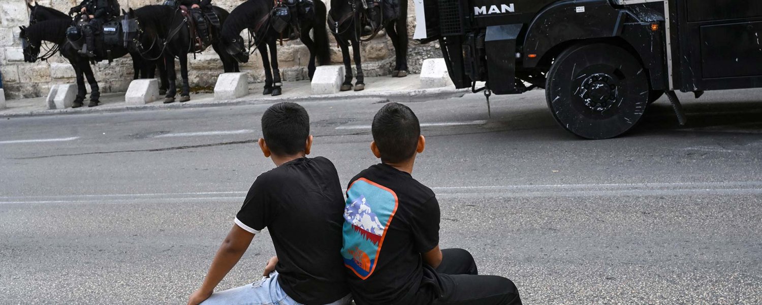 Two Palestinian children looking at Israeli soldiers on horses 