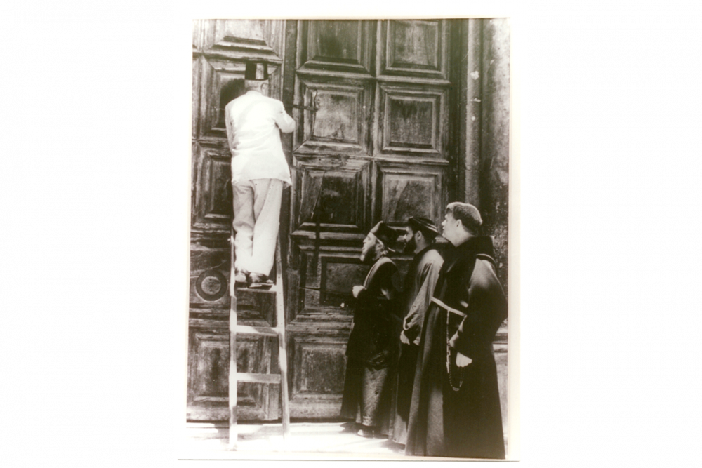 A member of the Nusseibeh family opens the door of the Church of the Holy Sepulchre as priests look on.