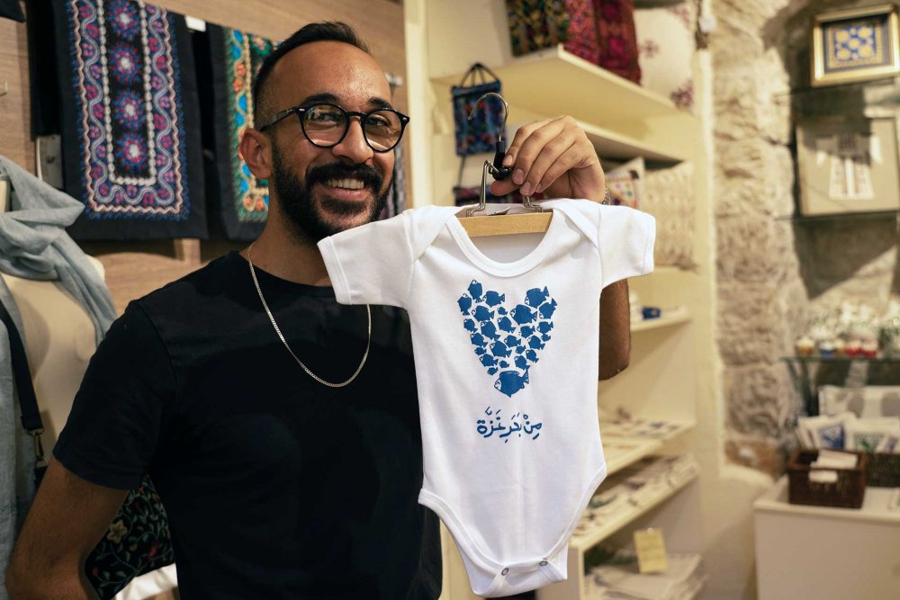 Sunbula employee holds a locally designed baby onesie at the Sunbula crafts store in Jerusalem, August 21, 2024.